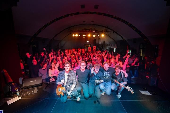 Fünf Bandmitglieder vor einer Menge jubelnder Konzertbesucher Fünf Bandmitglieder vor einer Menge jubelnder Konzertbesucher
