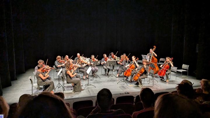 Ein Orchester spielt auf einer Bühne vor schwarzem Vorhang Ein Orchester spielt auf einer Bühne vor schwarzem Vorhang