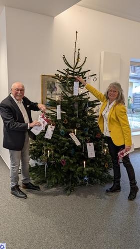 Eine Frau und ein Mann hängen Wunschzettel an einen Tannenbaum Eine Frau und ein Mann hängen Wunschzettel an einen Tannenbaum