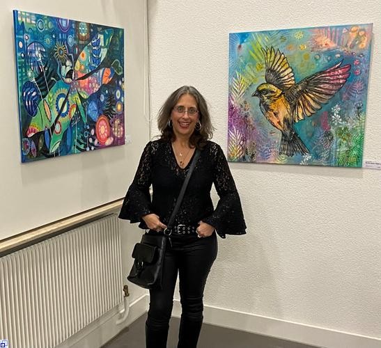 Eine Frau in schwarzer Kleidung steht zwischen zwei farbstarken Gemälden Eine Frau in schwarzer Kleidung steht zwischen zwei farbstarken Gemälden