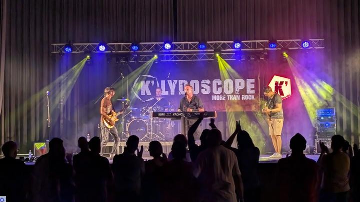 Eine farbig beleuchtete Bühne mit einer Band, davor tanzende Menschen