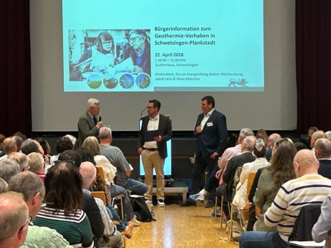 Drei Männer stehen vor einer Leinwand mit einer Präsentation im Publikum sitzen viele Menschen